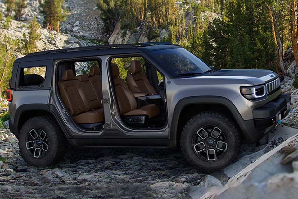 A photo of the rear of an all-electric Jeep Recon on a beautiful beach with cliffs and the surf in the background.