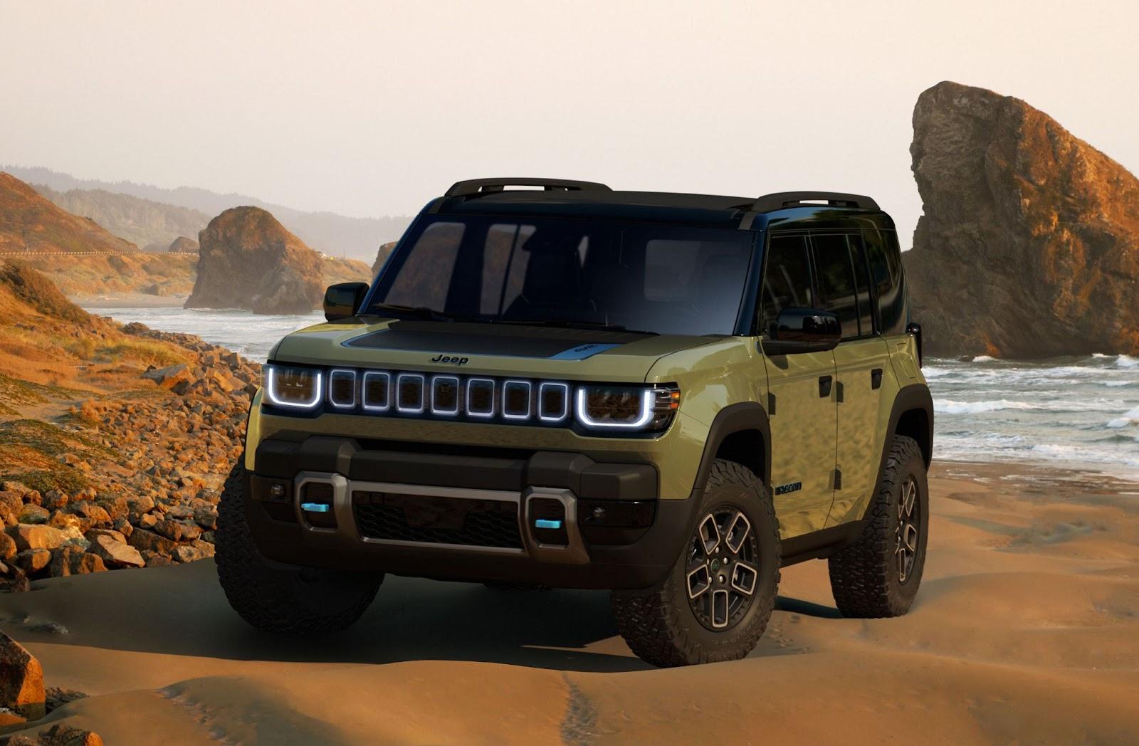 A 2025 Jeep Recon electric vehicle sits at the bottom of a rugged rocky hill with its doors removed, revealing its comfortable, modern interior.